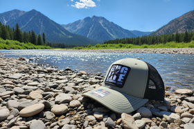 Buglife Fly Goods hat on bright Montana riverbank